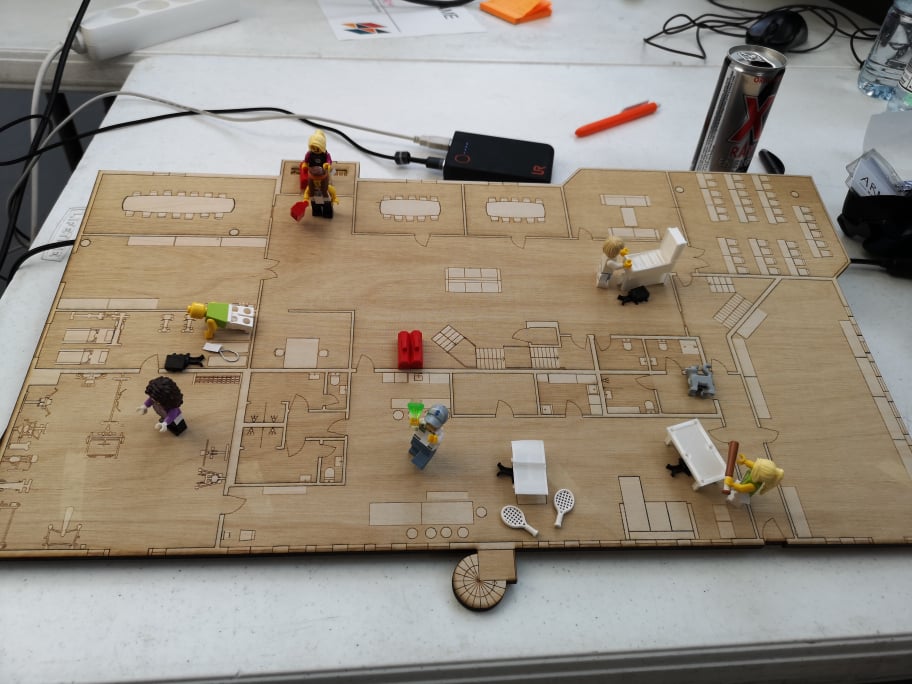 Picture of a lasercut building plan with 3D-printed points of interest and lego figures interacting.